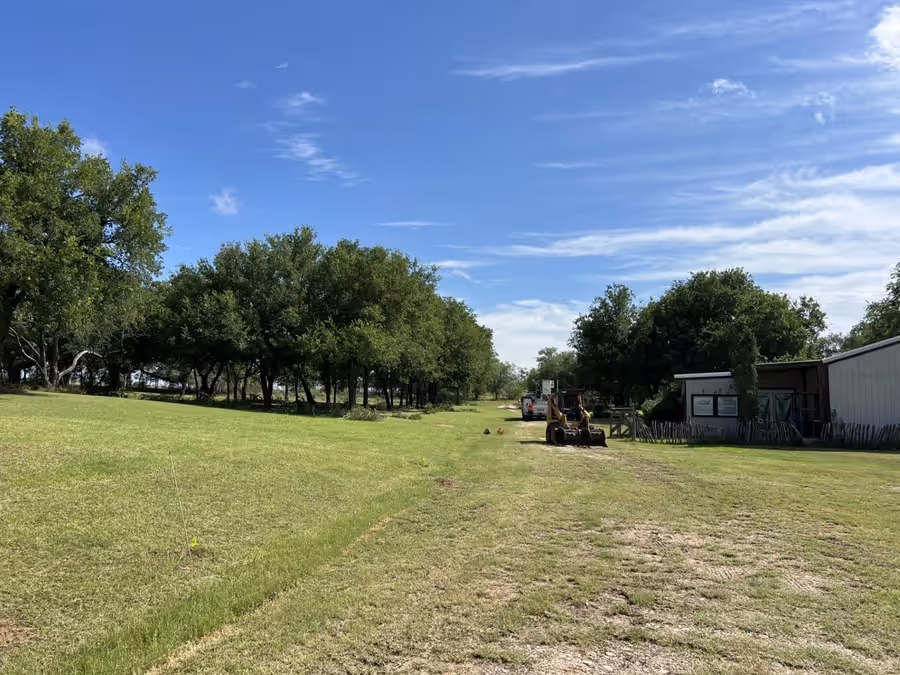 Skid steer and work truck clearing a treeline on open Hill Country acreage