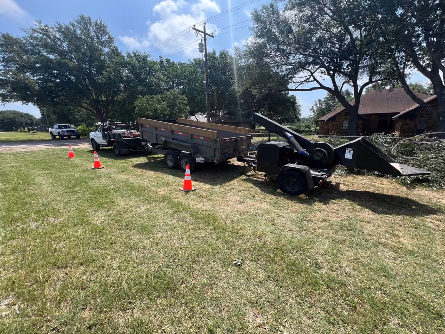 Work truck, dump trailer and chipper staged behind safety cones under overhead lines
