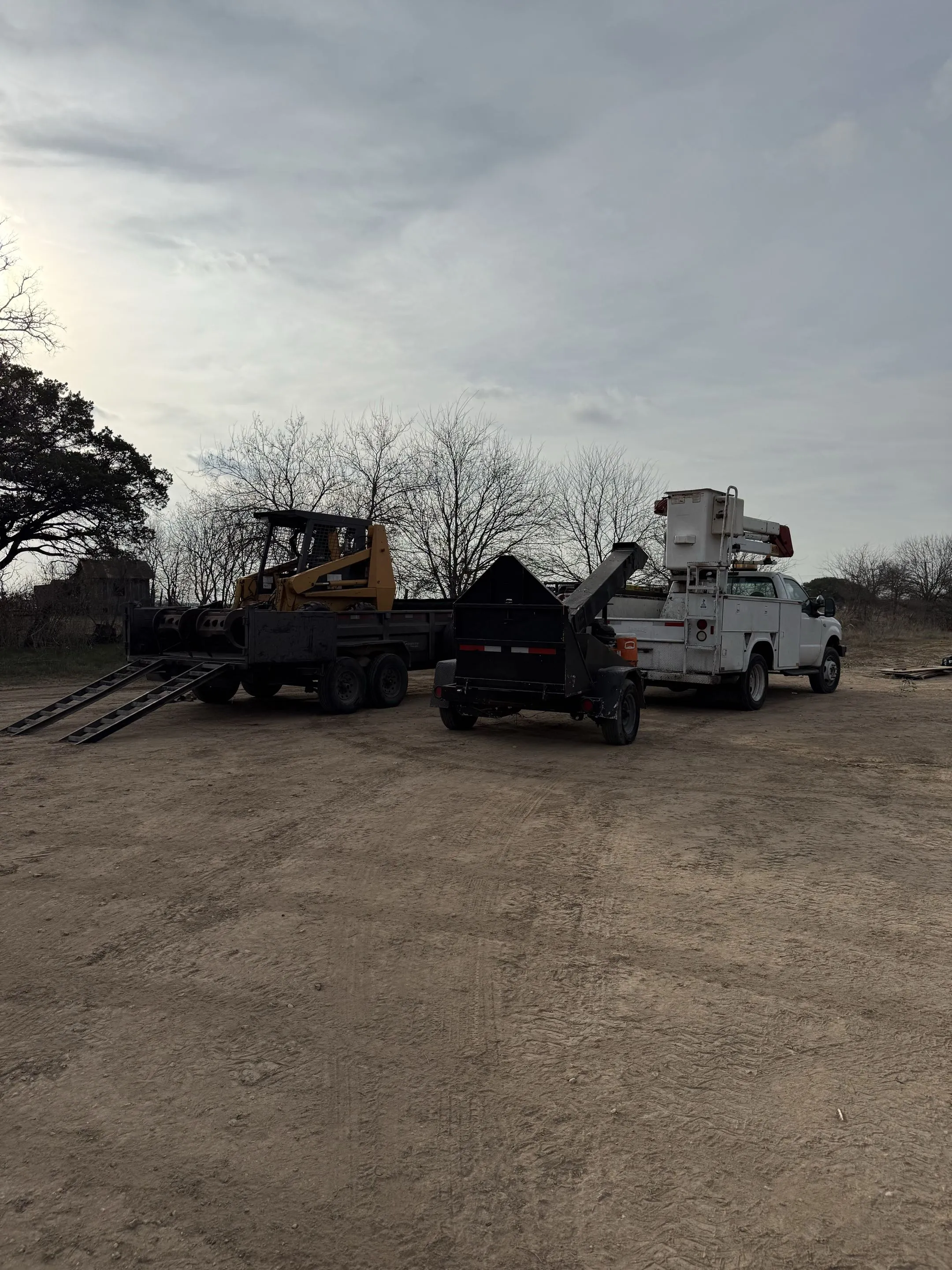 Skid steer, chipper and bucket truck loaded and staged for a job