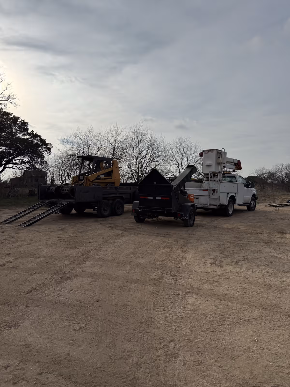 Skid steer, chipper and bucket truck loaded and staged for a job