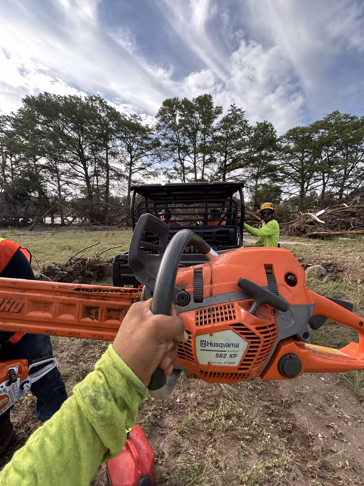 Gloved hand holding a chainsaw on a riverside storm cleanup