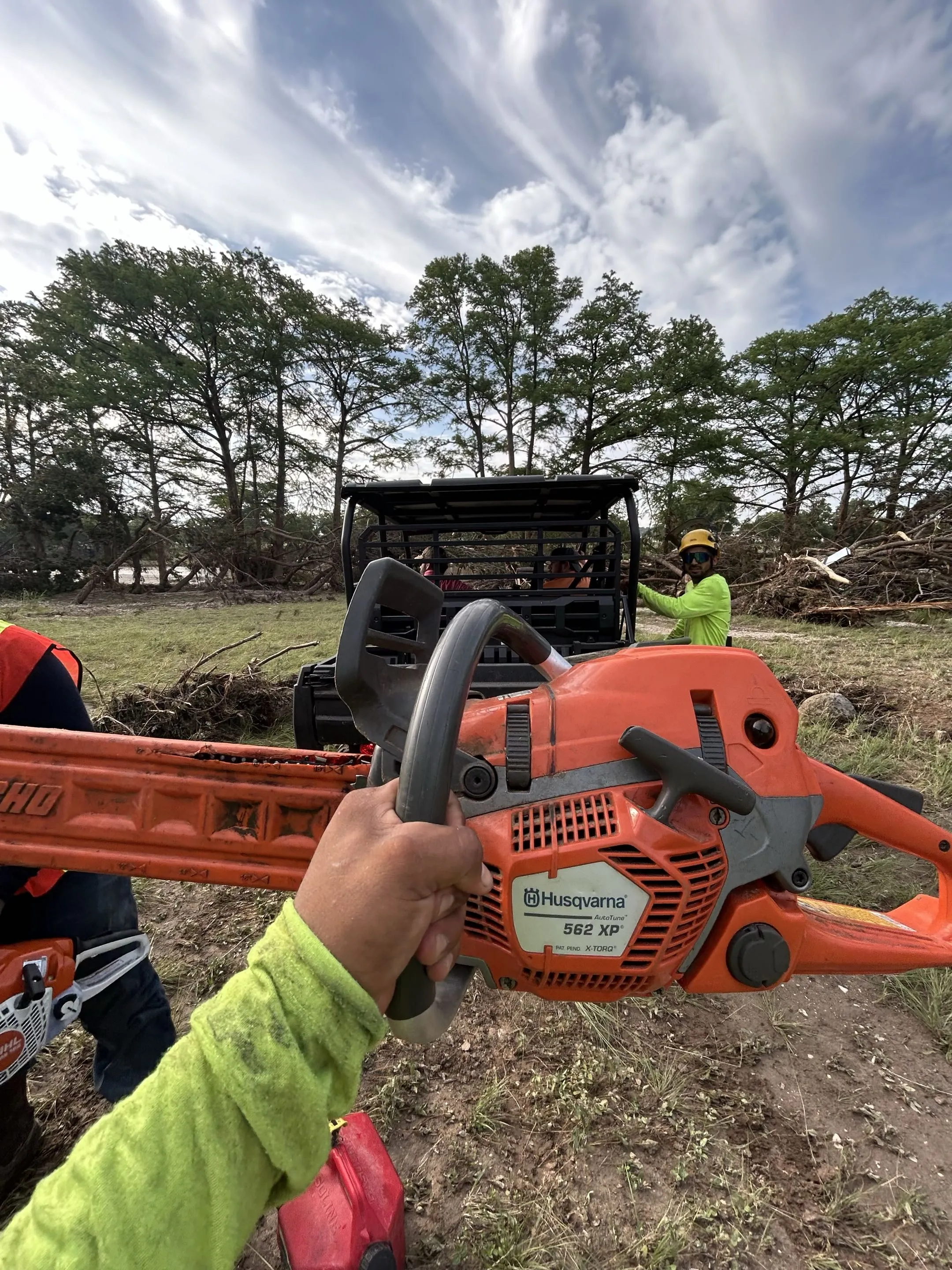 Gloved hand holding a chainsaw on a riverside storm cleanup