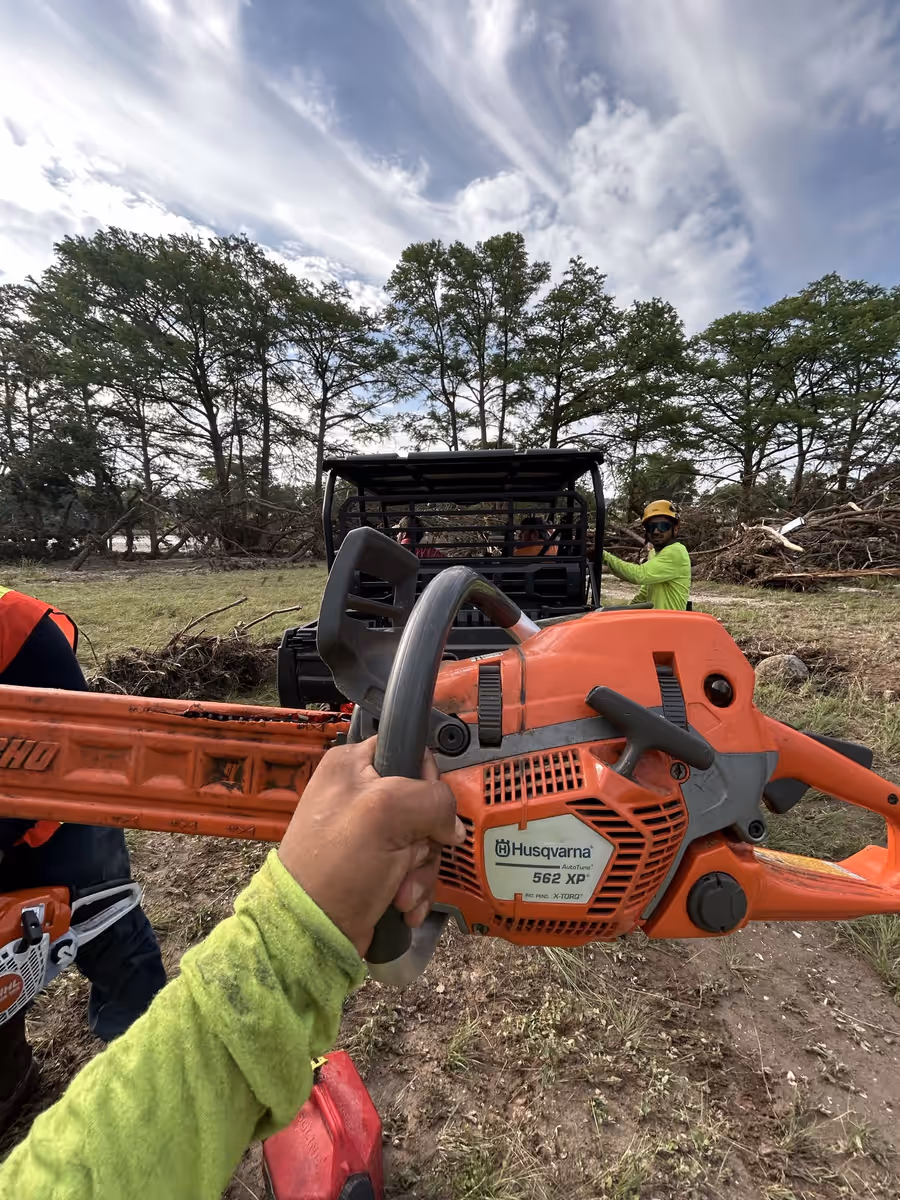 Gloved hand holding a chainsaw on a riverside storm cleanup